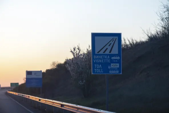 Bulgarian motorway sign at sunset showing vignette requirement for vehicles under 3.5t and toll for vehicles over 3.5t in Bulgarian and English